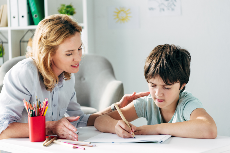 Tutor overlooking a young child writing on a piece of paper