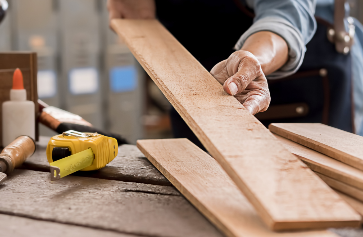 The hands of a tradesperson holding a long, rectangular piece of wood