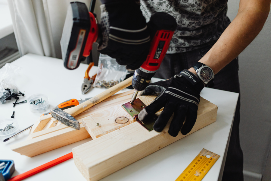 The hands of a tradesperson drilling a metal bracket onto a piece of wood
