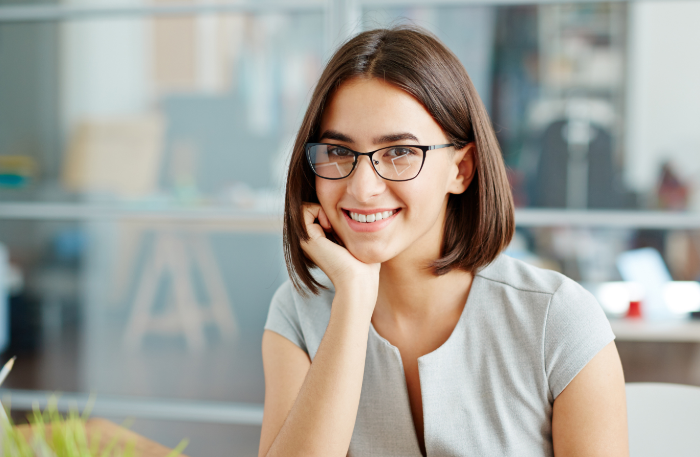 A professional wearing glasses, smiling as they lean on their hand
