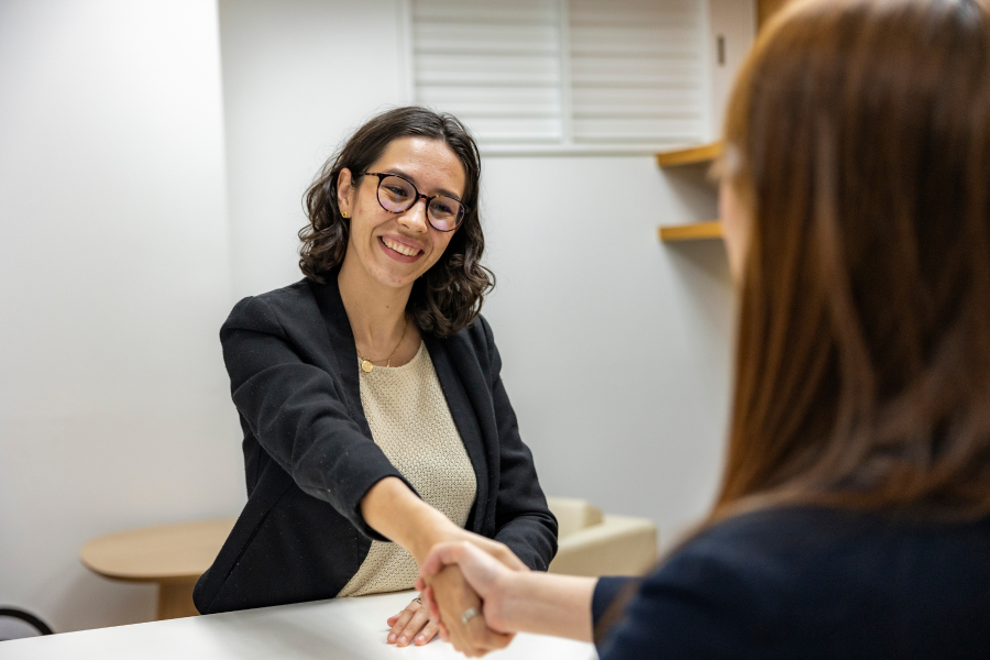 A professional smiling as they shake hands with an individual sat opposite them