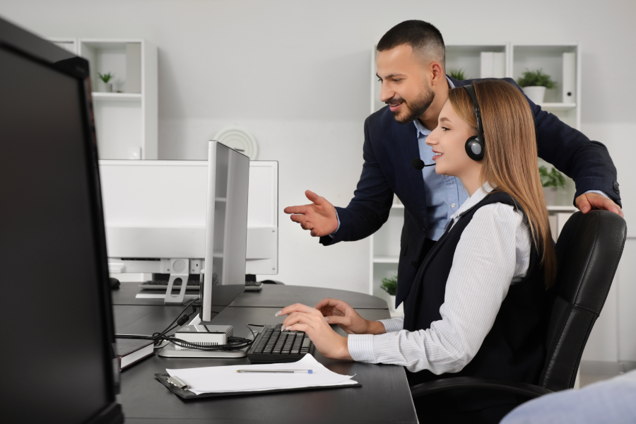 Two professionals looking at a computer screen, one wears a microphone headset