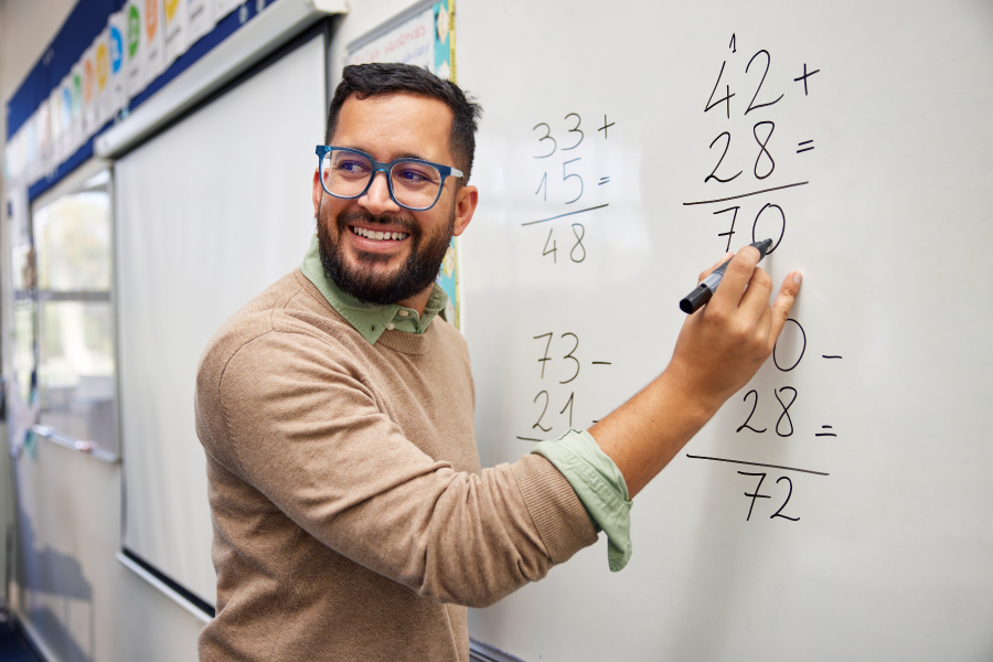 A professional stood in a classroom, writing maths equations on a whiteboard