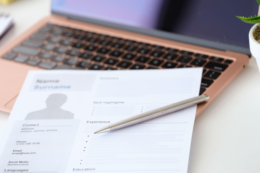 A laptop, pen and CV template on a table