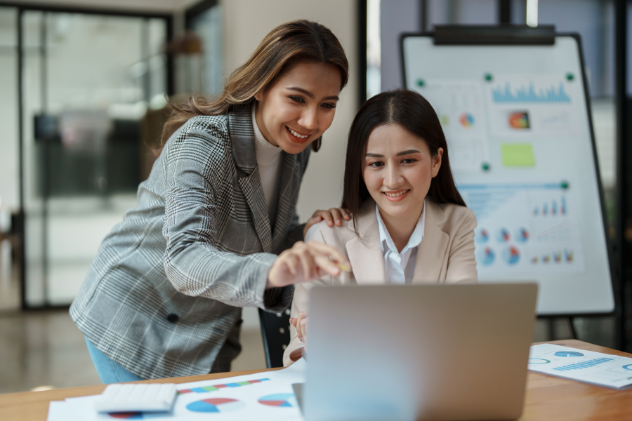 Two professionals in an office looking at a laptop screen, one of them stood and the other person sat