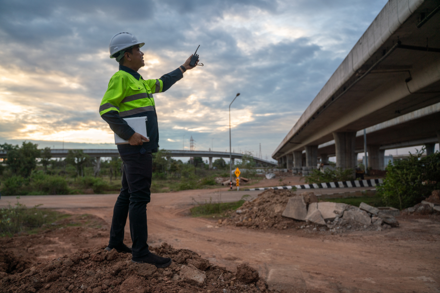 A professional in a green high vis jacket and white hard hat, pointing at a bridge structure
