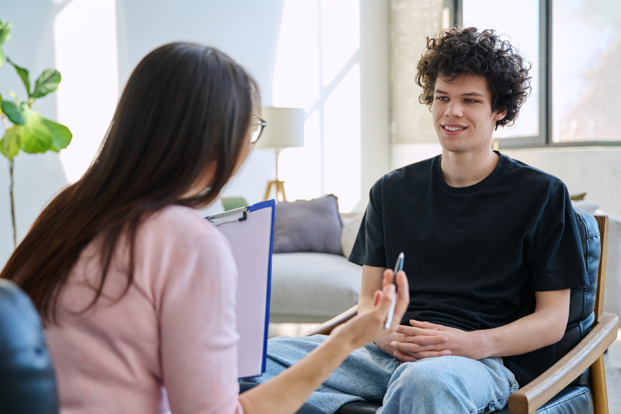 A professional sat with a young person, speaking as they hold a pen and clipboard
