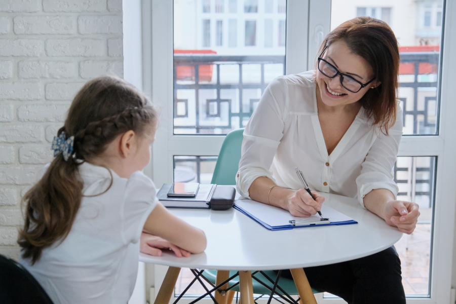 A professional sat with a young child, writing on paper attached to a clipboard
