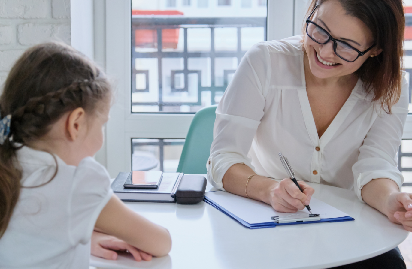 A professional sat with a young child, writing on paper attached to a clipboard