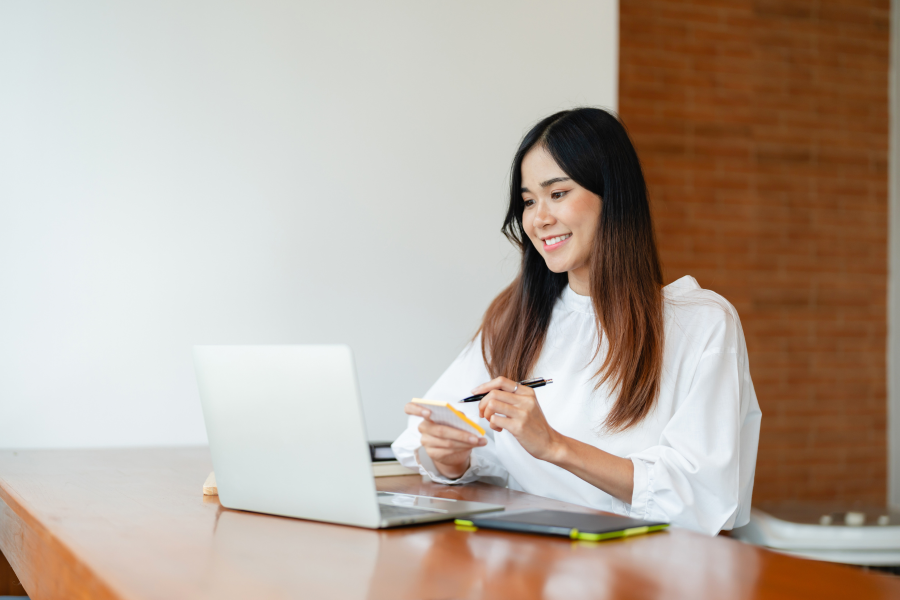 A professional sat in front of a laptop, poised ready to write on a piece of paper