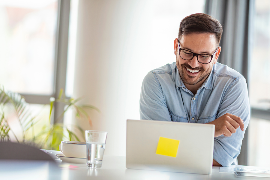 A professional wearing a blue denim shirt and glasses, smiling at a laptop