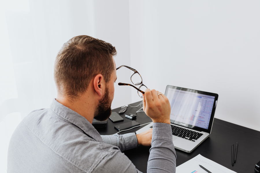 The back of a professional holding their glasses, as they type on a laptop
