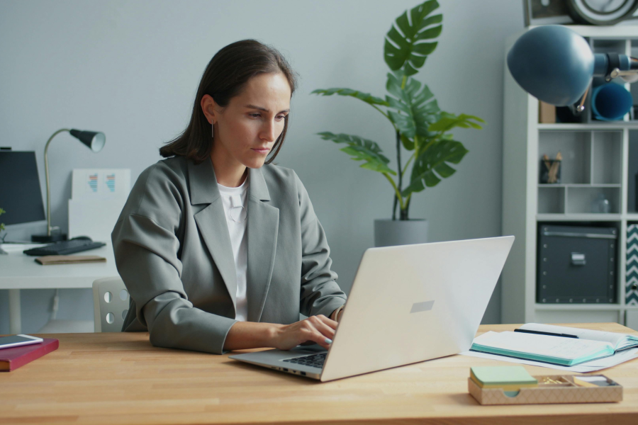 A professional sat in an office, wearing a grey blazer and using a laptop