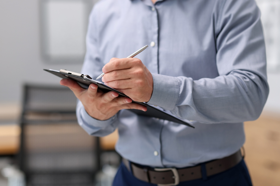 The torso of a professional wearing a blue shirt, writing on a clipboard