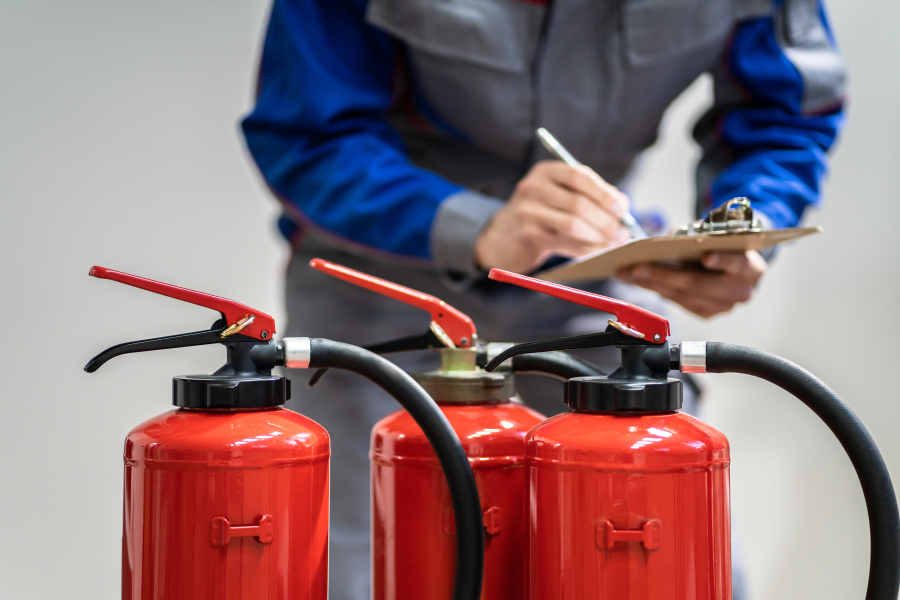 Three fire extinguishers lined up as a professional behind them writes on a clipboard