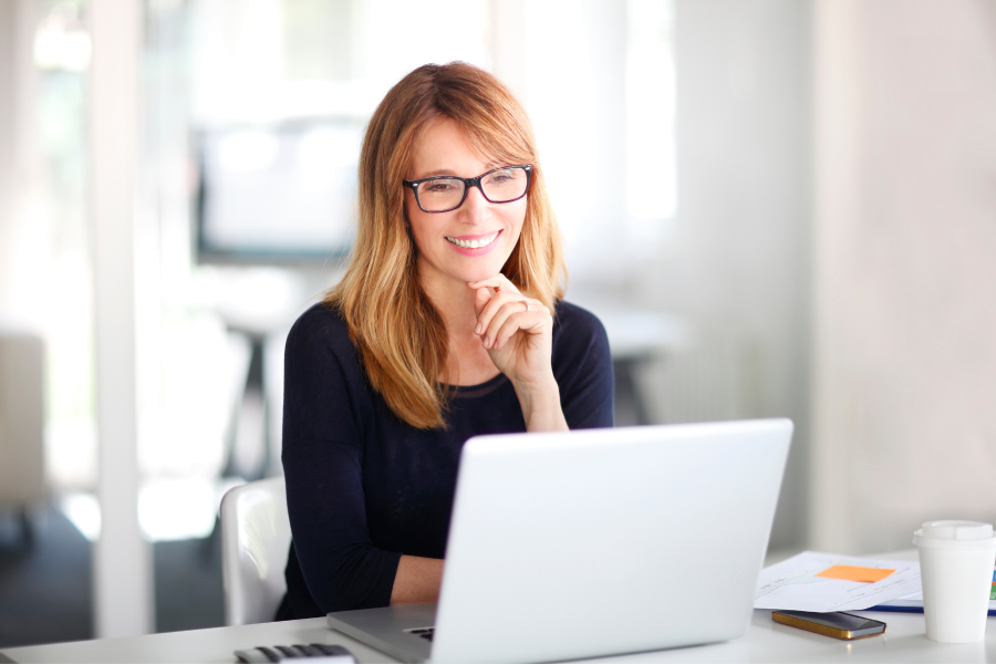 A professional wearing glasses smiling as they work on their laptop