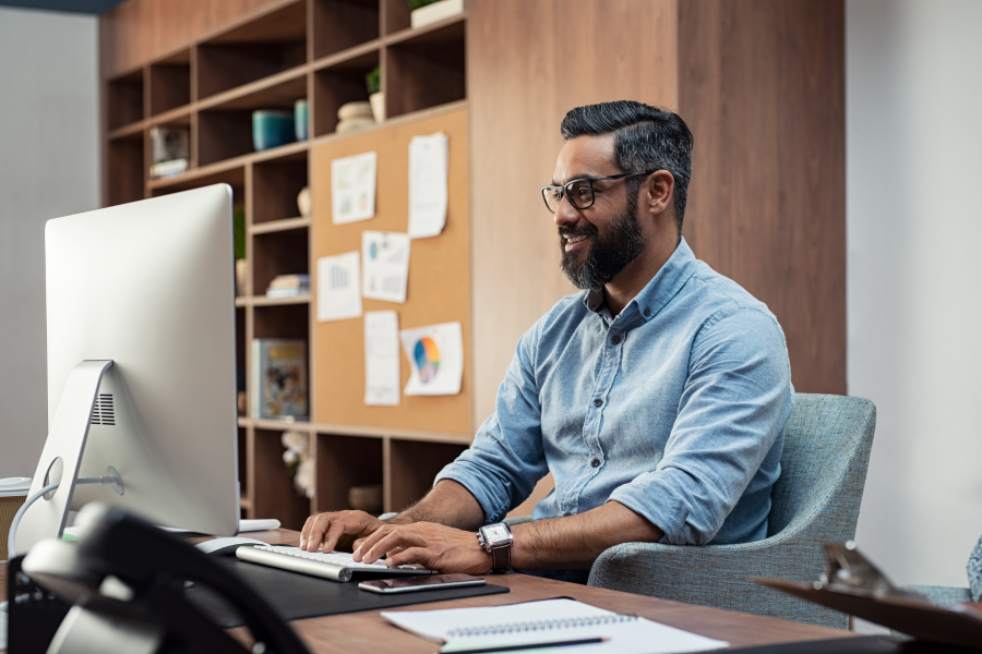 A professional wearing a blue shirt smiling whilst typing on their computer