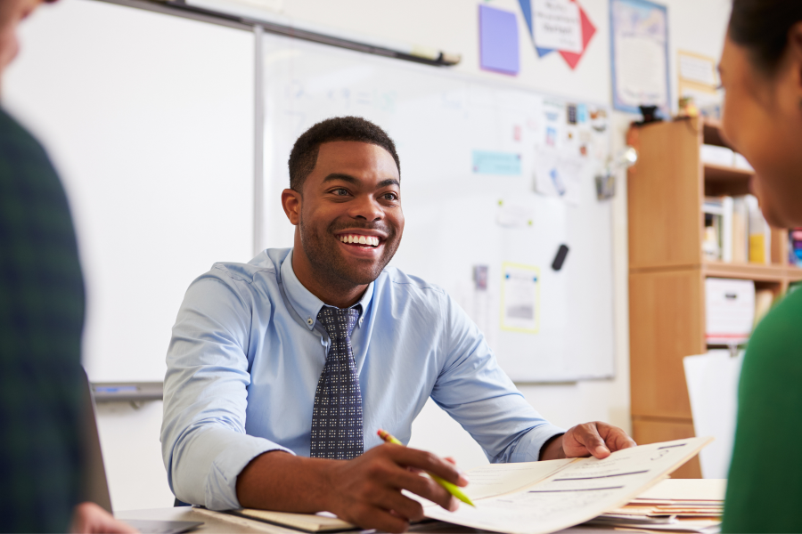 A professional smiling at a person opposite whilst holding a pen and piece of paper