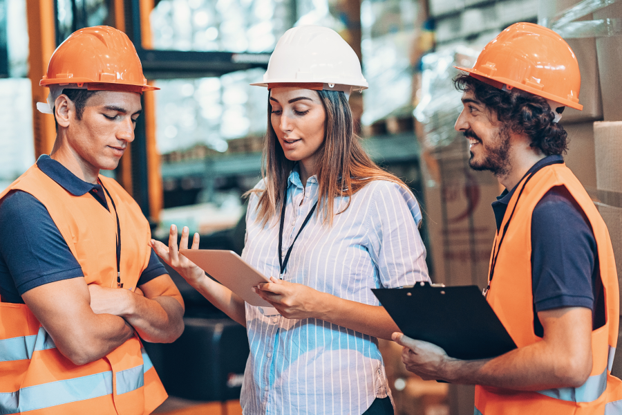 Three workers wearing hard hats standing looking at a digital device