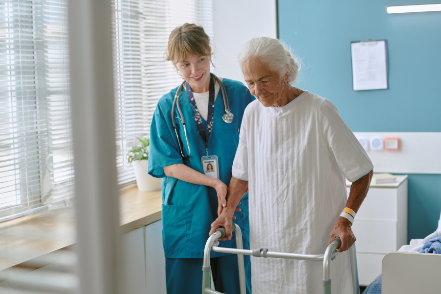 A healthcare professional helping an elderly patient walk with a zimmer frame