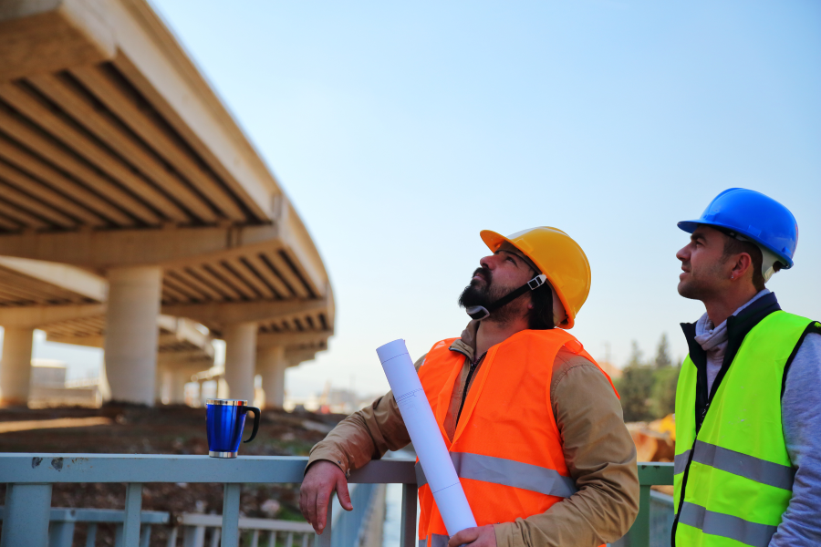 Two construction workers wearing high vis vests looking up at a concrete structure