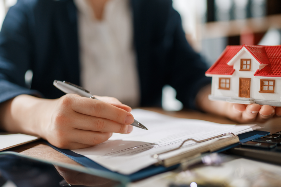 An adult writing on a piece of a paper holding a model of a house