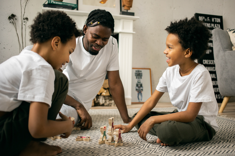 Two children and an adult sit on the floor playing with wooden toys