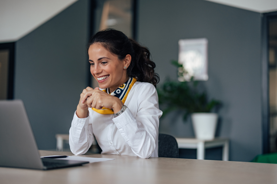 A professional sitting at a desk, smiling as they look at a laptop screen
