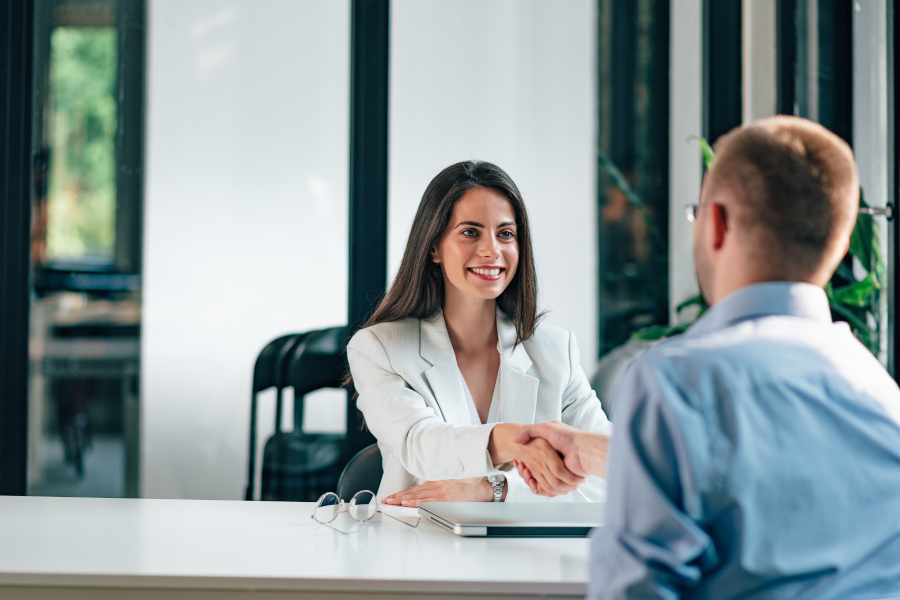 Two people shake hands across a desk