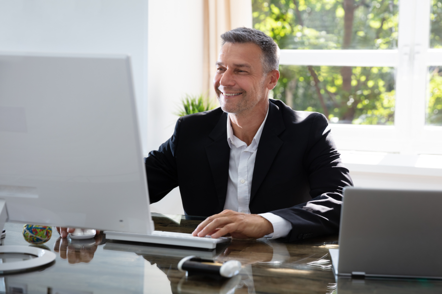 A professional wearing a white shirt and black blazer smiling at their computer screen