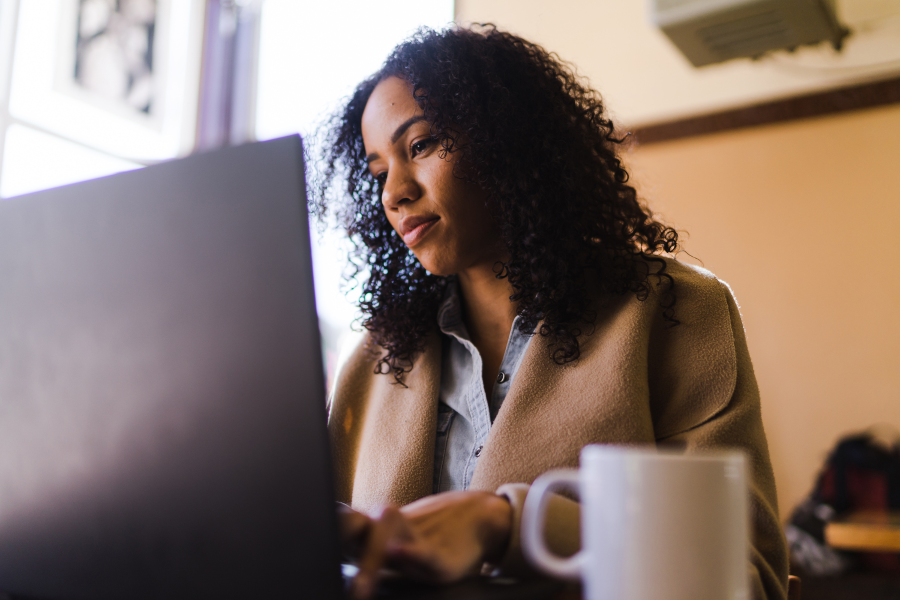 A professional looking at their laptop screen with a hot drink in a mug by them