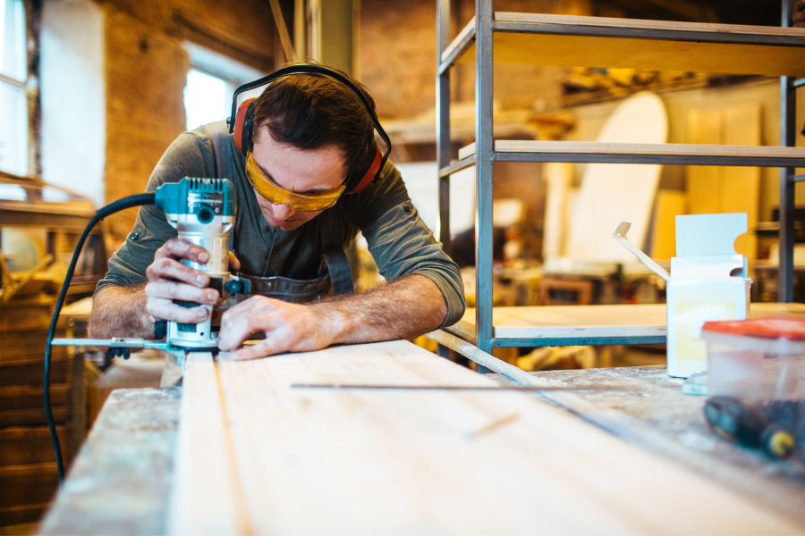 A tradesperson sawing a piece of wood whilst wearing protective glasses and ear defenders