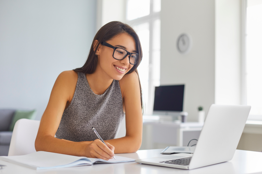 A professional wearing glasses and a grey top smiling and writing in a notebook