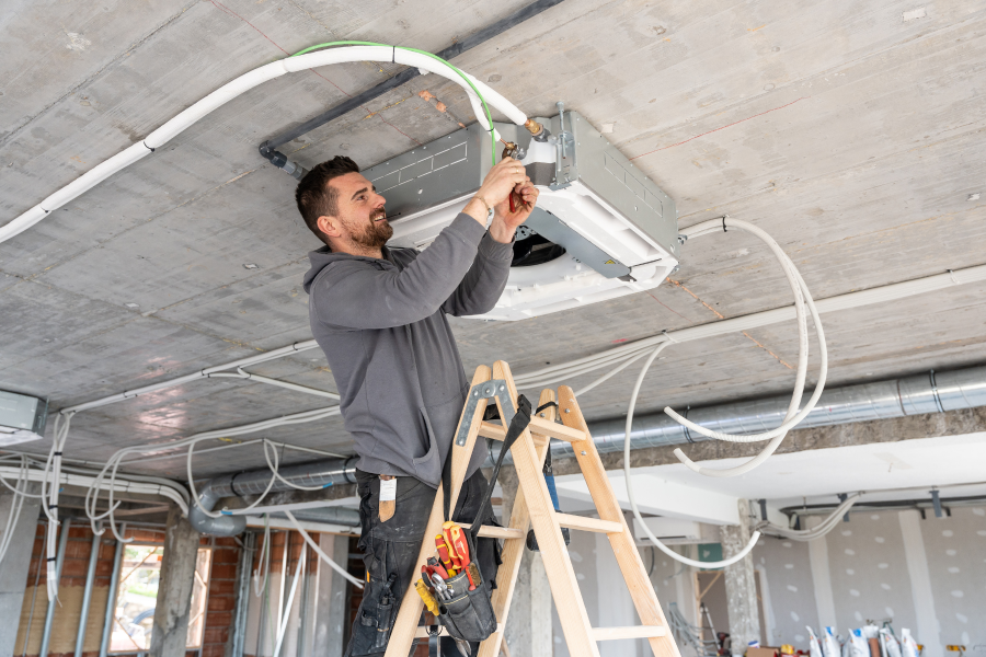 A tradesperson standing on a ladder fixing an air conditioning unit