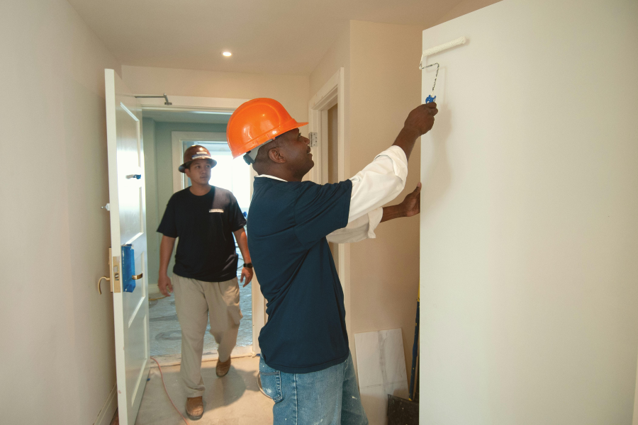 A tradesperson wearing an orange hard hat painting a wall