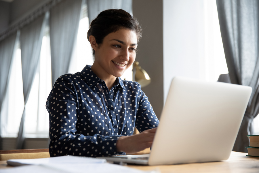 A professional wearing a navy top with white spots, smiling at a laptop screen