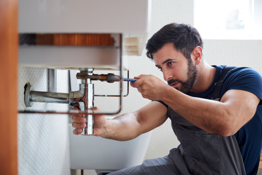 A tradesperson completing plumbing work under a sink