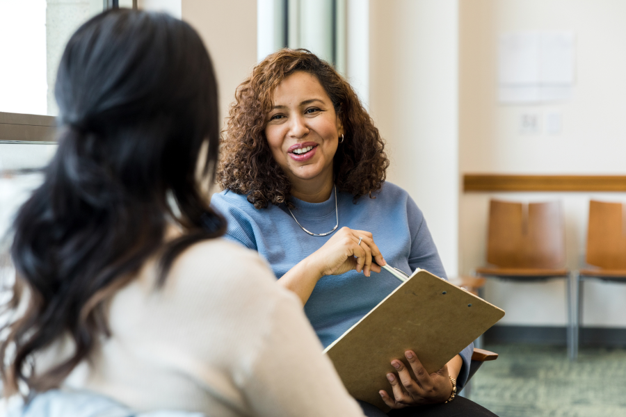 Two people sat chatting whilst one is holding a pen and clipboard