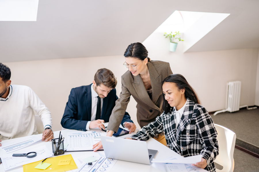 Four professionals sat working at a desk amongst a laptop and pieces of paper