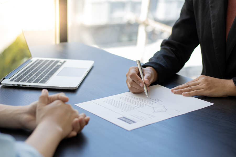 Two adults sat at a desk with a laptop and with one adult writing on a piece of paper