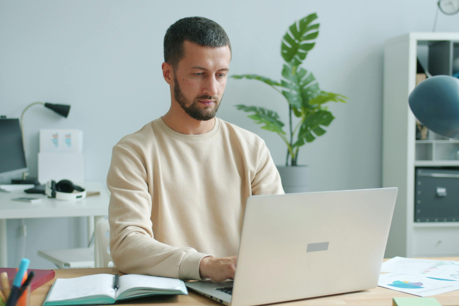A professional wearing a beige jumper sitting typing on their laptop