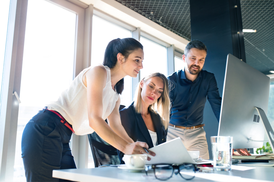 Three professionals in an office gathered looking at a desktop screen