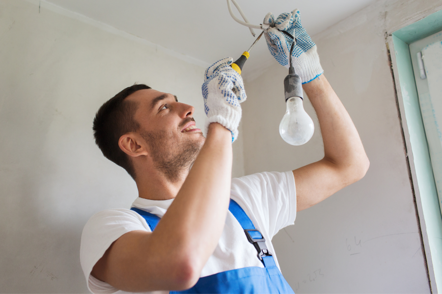 A tradesperson fixing a light bulb that is hanging from the ceiling