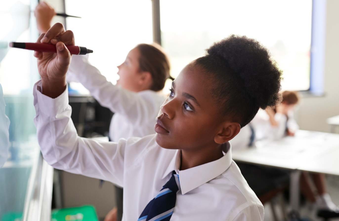 A school student wearing a white shirt and striped tie writing on a digital smartboard