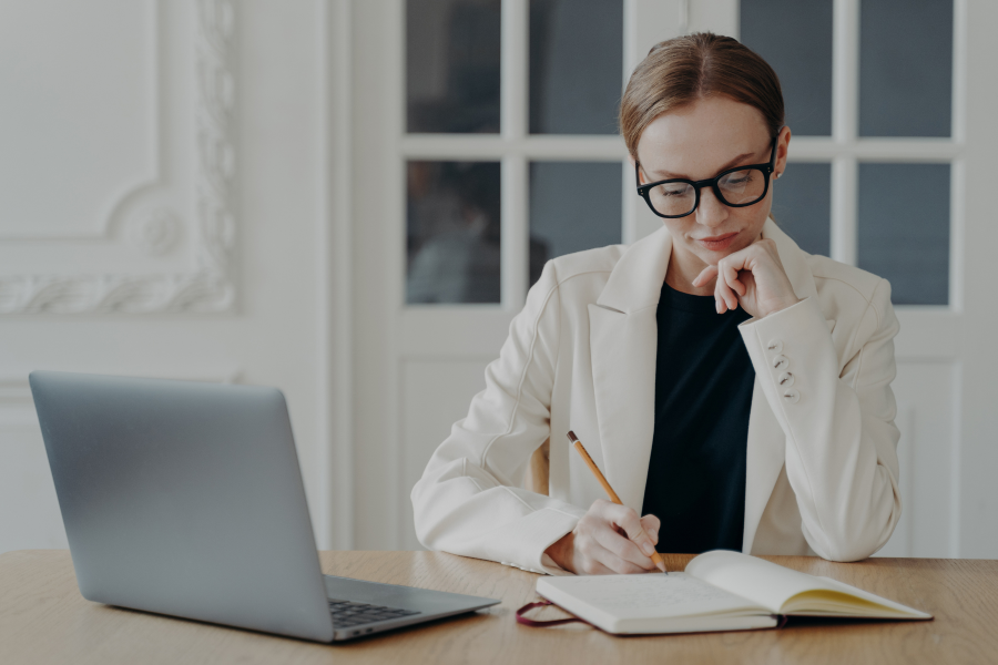 A professional wearing glasses, sitting writing into their notebook
