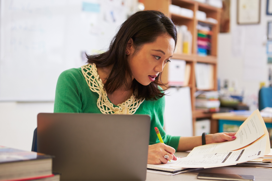 A professional wearing a green jumper, sitting at a desk writing