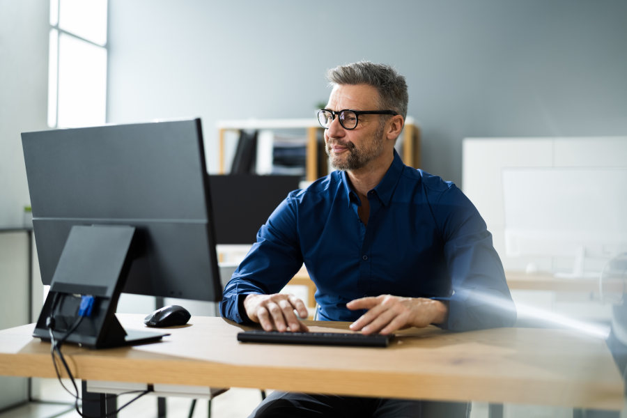 A professional wearing a navy blue shirt and glasses, looking at their desktop computer