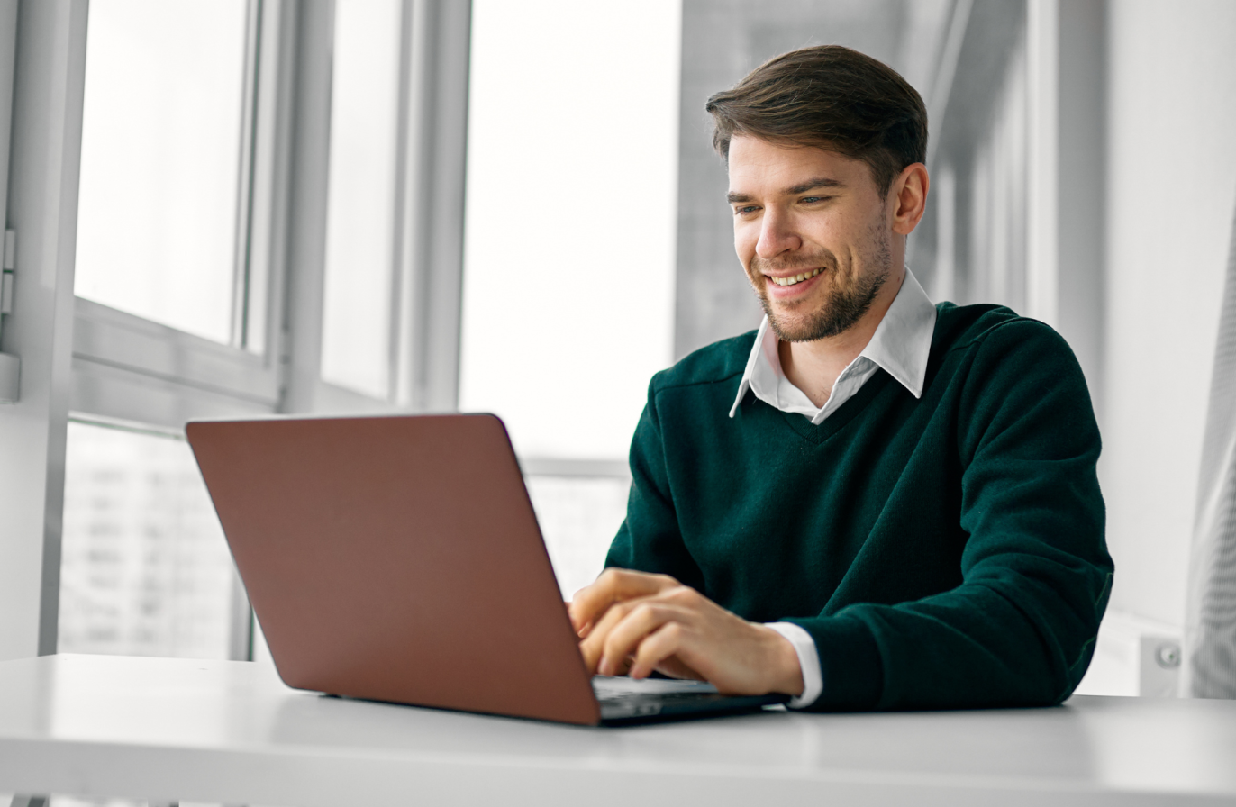 A professional wearing a green jumper, smiling and looking at their laptop