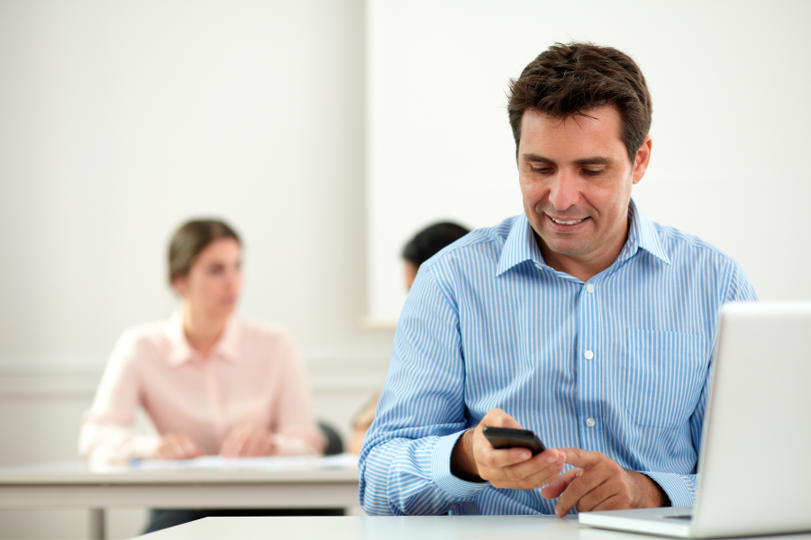 A professional in a blue striped shirt, looking at a mobile phone