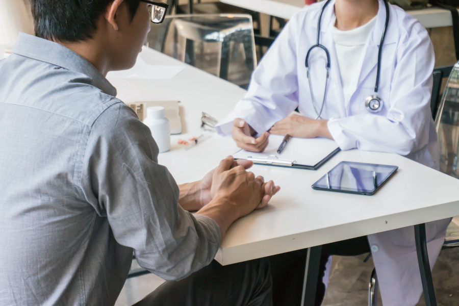 The torso of a healthcare professional sitting opposite a person in a grey shirt